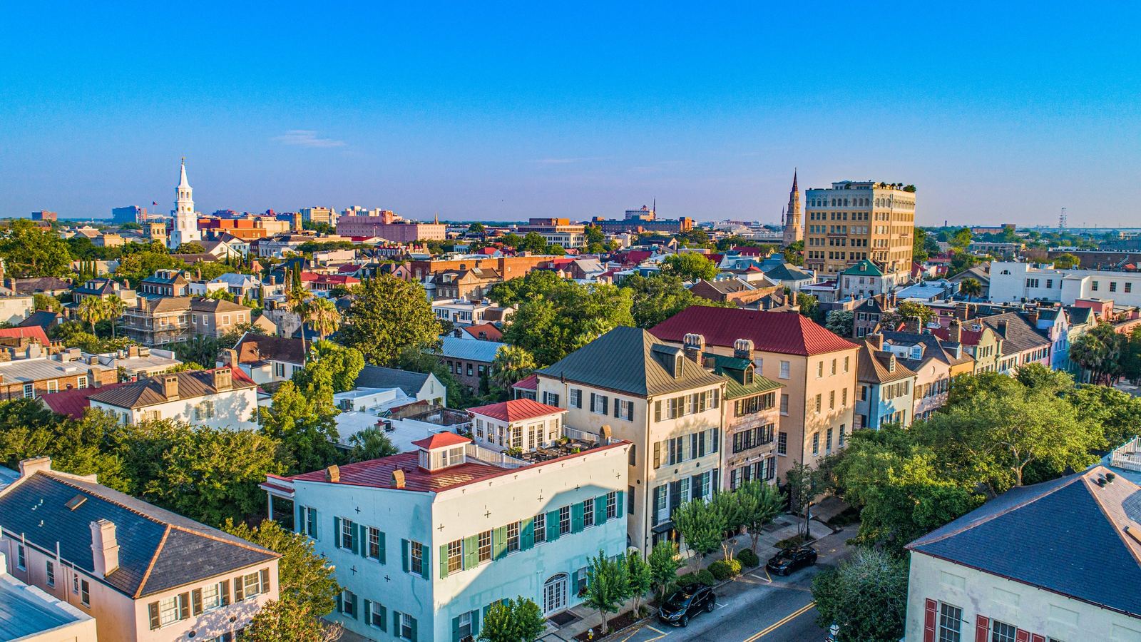 Aerial view of historic downtown Charleston, South Carolina, with colorful rooftops, church steeples, and tree-lined streets